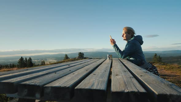 A Woman Sits at a Table Uses Her Phone High in the Mountains of Norway alt