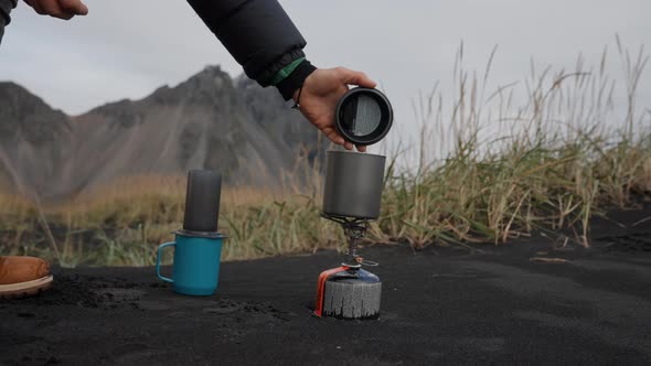 Man Removing Lid From Cup On Camp Stove On Beach alt