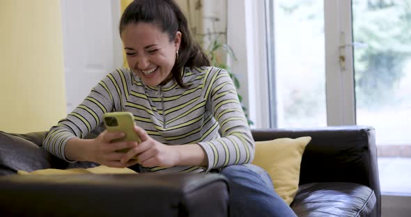 Woman using mobile phone on the sofa and celebrating success or victory onlin