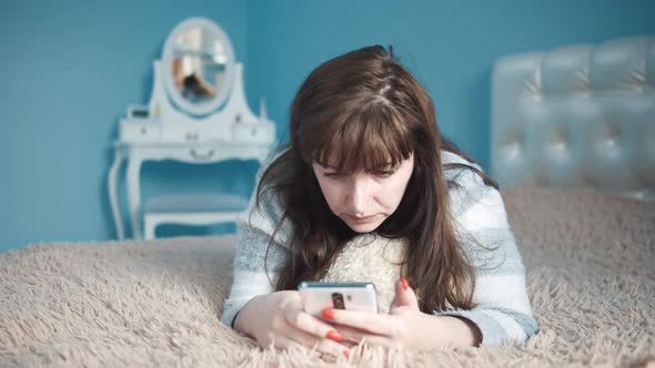Sad Woman Lies on the Bed and Uses the Phone Text Messages with Friends Problems
