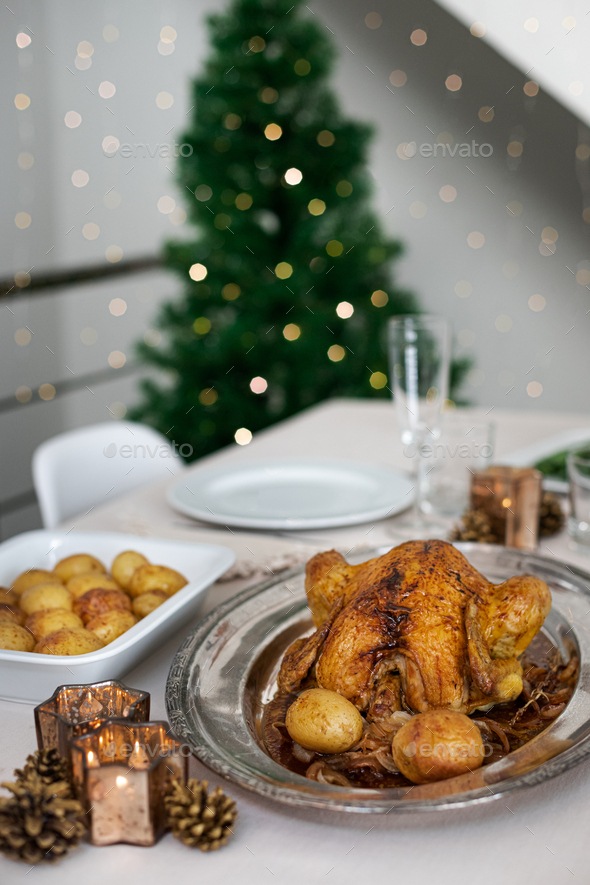 Christmas dinner minimalist table setting with roasted chicken and christmas tree on background.