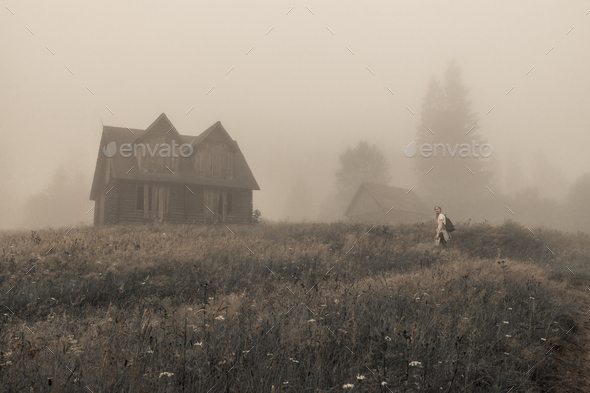 Old wooden shabby house or building in a misty mystical field in a green eco forest. Woman tourist