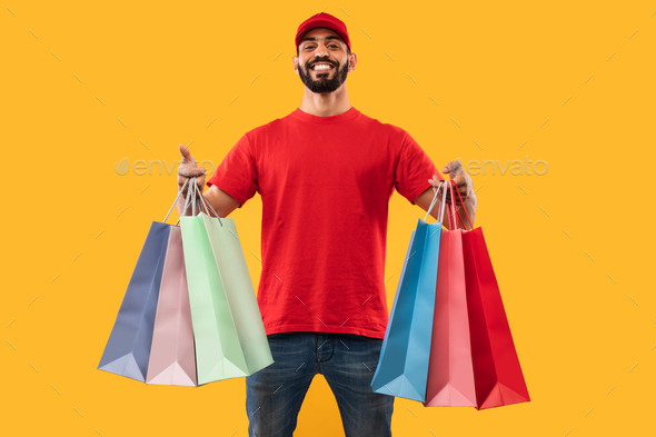 Arabic Courier Guy Offering Shopping Bags To Camera, Yellow Background