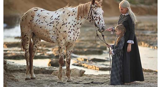 little girl her mom on the beach with a horse