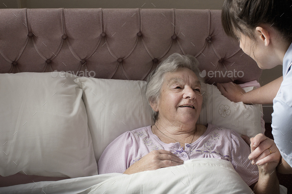 Personal care assistant chatting to senior woman in bed