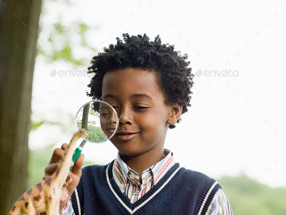 A boy looking at a toy dinosaur with a magnifying glass