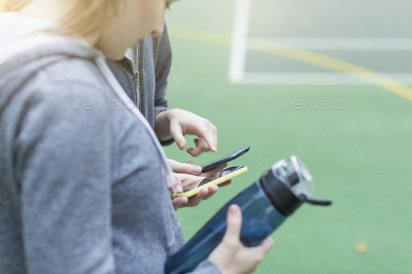 Cropped side view of young woman on sports court holding water bottle looking down at smartphone