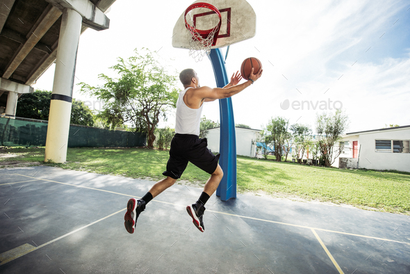 Side view of young man on basketball court in mid air holding basketball jumping for hoop