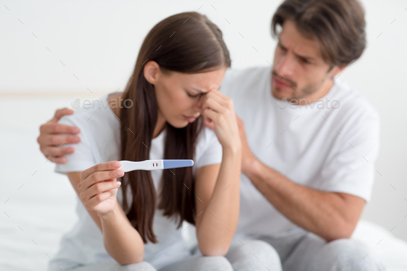 Despaired sad millennial european husband calms, support his wife, lady hold pregnancy test