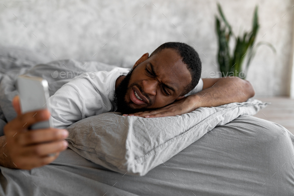 Black man suffering from insomnia looking at phone in bed