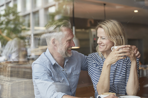 View through window of mature couple in coffee shop face to face smiling