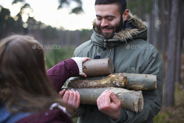 Young hiking couple collecting logs for campfire in forest