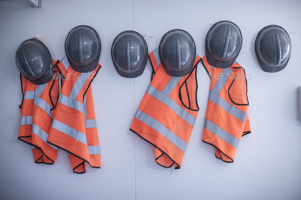 Rows of hard hats and high vis jackets on portable cabin wall