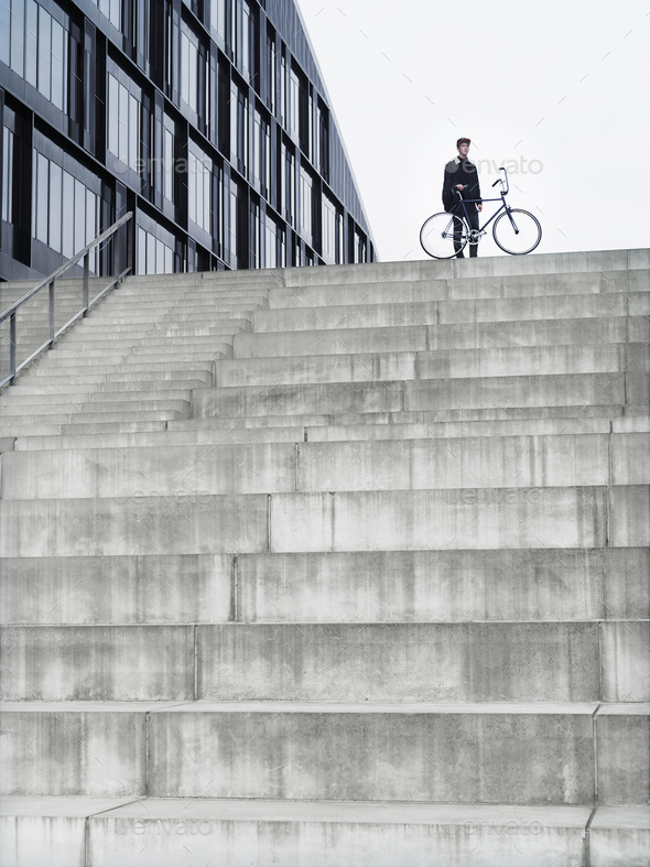 Urban cyclist with bicycle standing on top of stairway