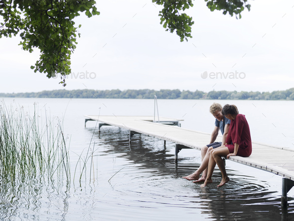 Couple sitting on pier side by side dipping toes in water, Copenhagen, Denmark