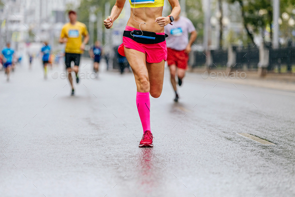 legs female runner in pink compression socks run in rain on wet road marathon