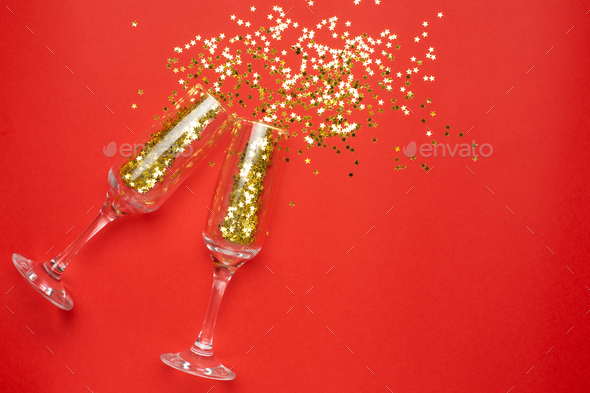Champagne glasses with golden stars confetti on red color paper