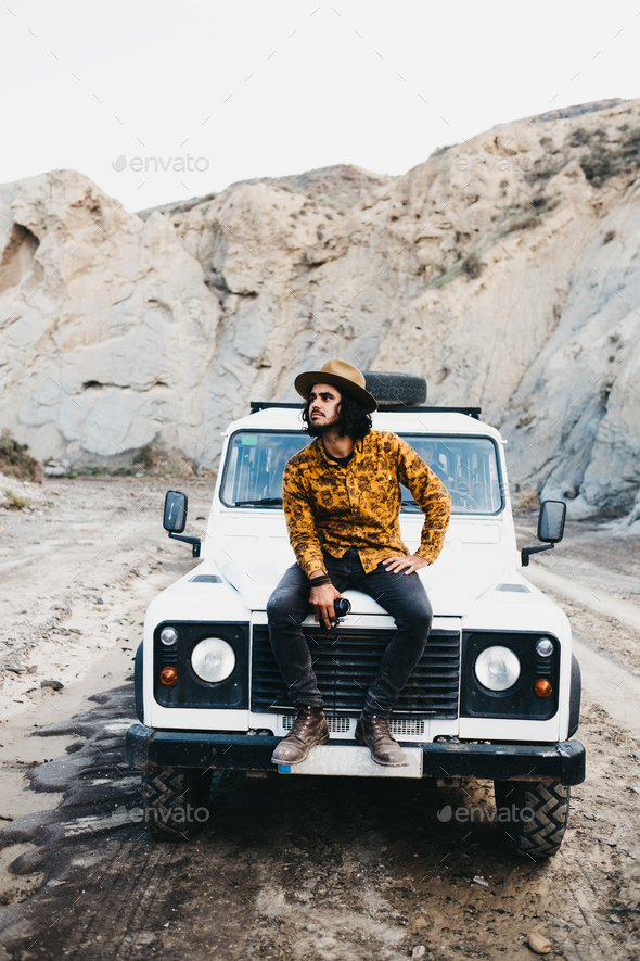 Stylish man sitting on car in canyon