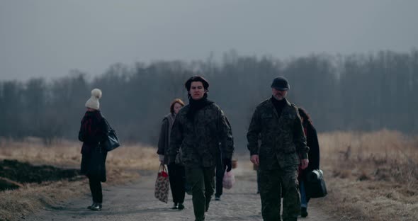 Military Soldiers Walking Ahead Of Refugee Group On Road alt