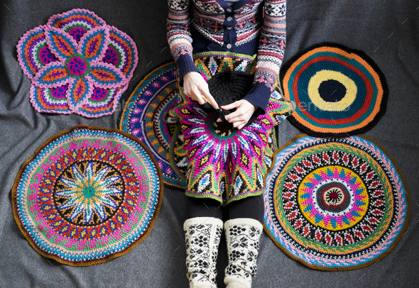 Neck down view of woman sitting on floor crocheting, surrounded by crochet circles