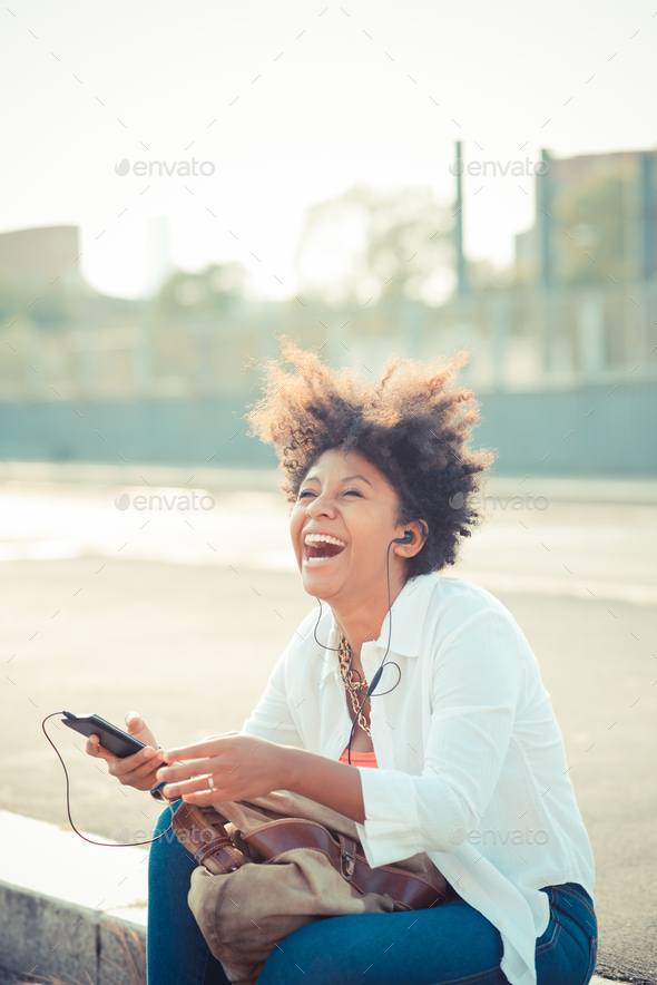 Young woman laughing and listening to smartphone music in city parking lot