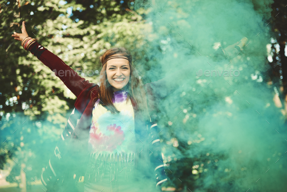 Young boho woman dancing with green smoke flare at festival
