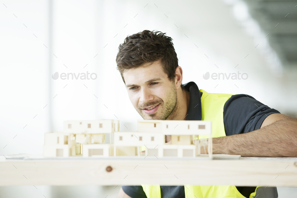 Man wearing hi vis vest, looking at model of building