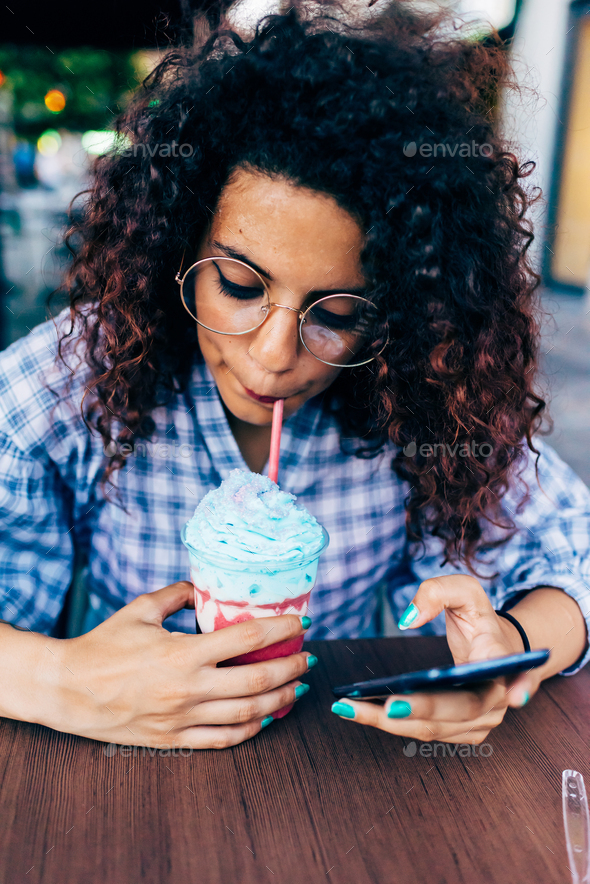 Woman using mobile phone while enjoying icy drink