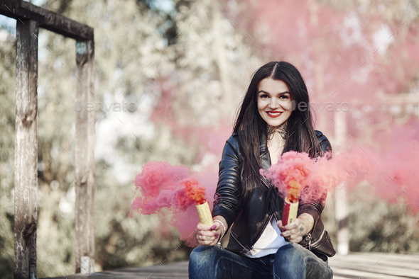 Young woman sitting on decking, holding smoke flares, smoke pouring from flares