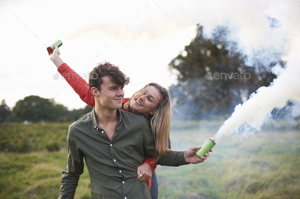 Young couple letting off smoke flares in field