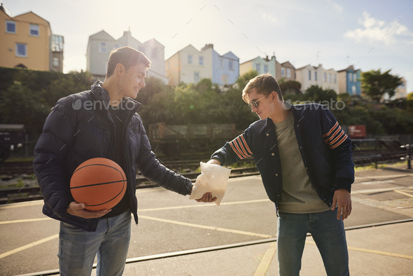 Young man sharing bag of chips with friend, young man holding basketball, Bristol, UK