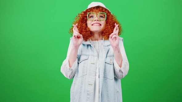 Young Funny Redhead Curly Woman in Glasses and Panama Hat Making Cherished Wish Crossing Fingers alt