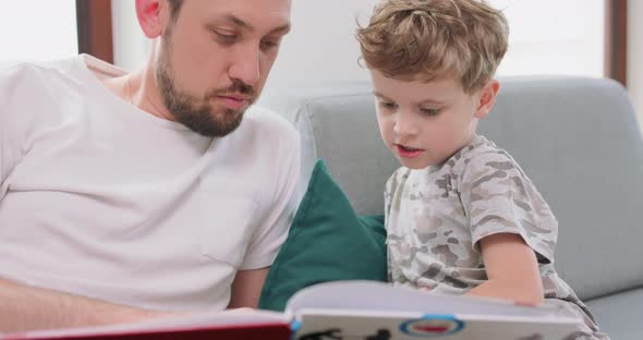 Close Up of Father and Son are Spending Time Together at Home By Reading a Book on the Sofa and alt