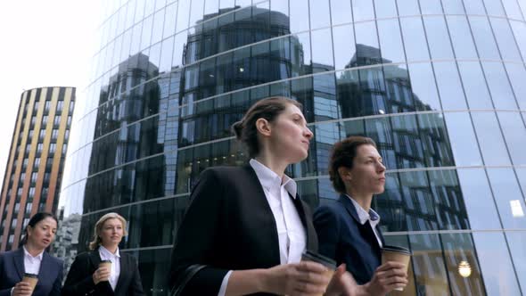 Low Angle View of Female Business Group Walking Through Modern Office Building. Drinking Coffee
