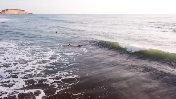 Surfers Paddling In Ocean With Breaking Waves Near Olon Beach In Summer.  - aerial alt