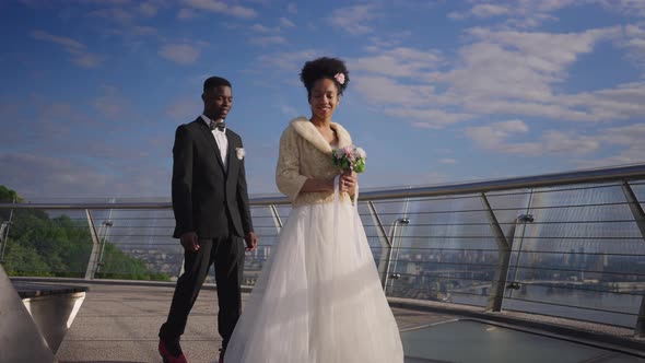 Happy African American Gorgeous Bride in Wedding Dress Holding Bridal Bouquet As Groom Approaching alt