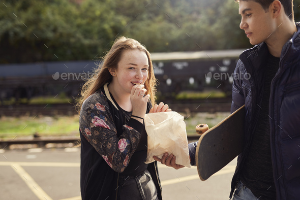 Young man sharing bag of chips with young woman, skateboard under young man\'s arm, Bristol, UK