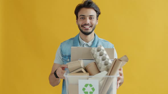 Slow Motion Portrait of Responsible Arab Guy Holding Box of Cardboard with Recycling Symbol alt