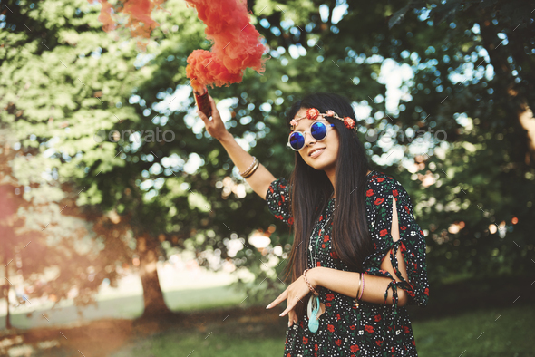 Young boho woman holding up red smoke flare at festival