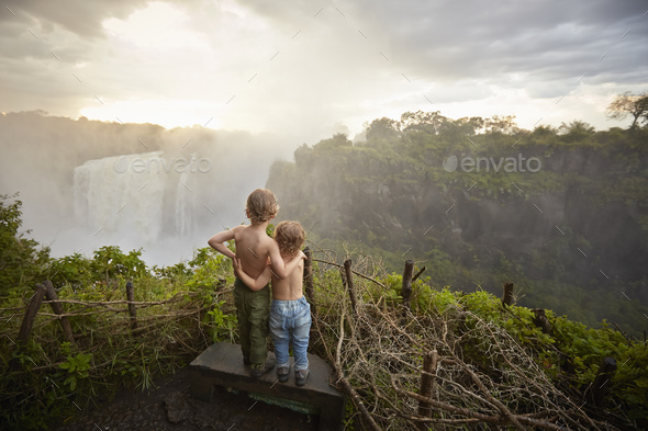 Two young boys standing on ledge admiring the view, rear view, Victoria Falls, Livingstone, Zimbabwe