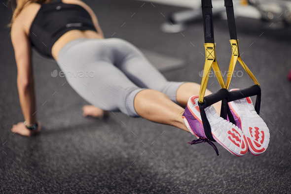 Neck down view of young woman doing push ups using exercise handles in gym