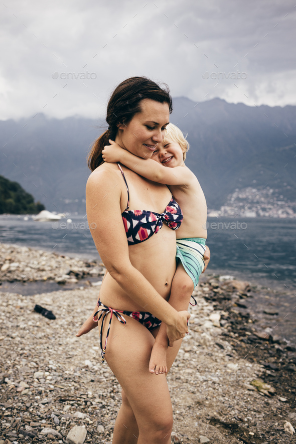 Mother by lake wearing bikini holdings smiling son, Luino, Lombardy, Italy