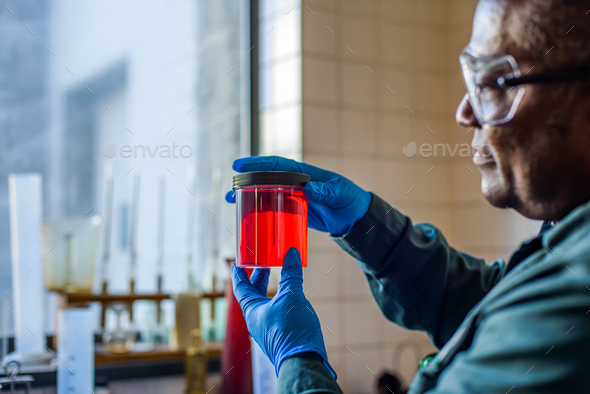 Lab technician looking at beaker of red biofuel in biofuel plant laboratory