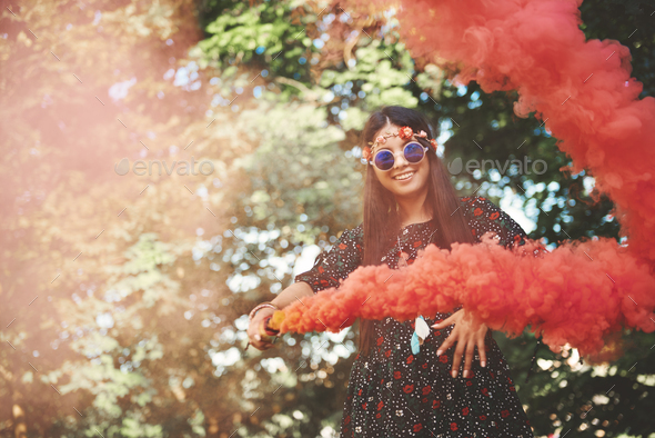 Young boho woman dancing with red smoke flare at festival