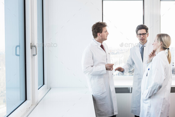 Three people wearing lab coats standing having conversation