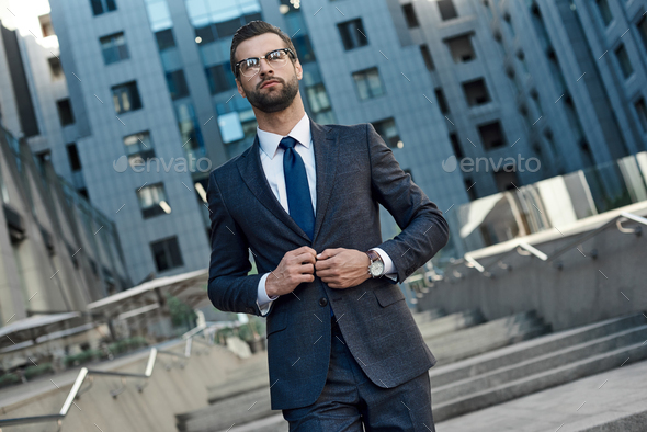 A young businessman fastens a suit jacket. He has on his hands an expensive watch