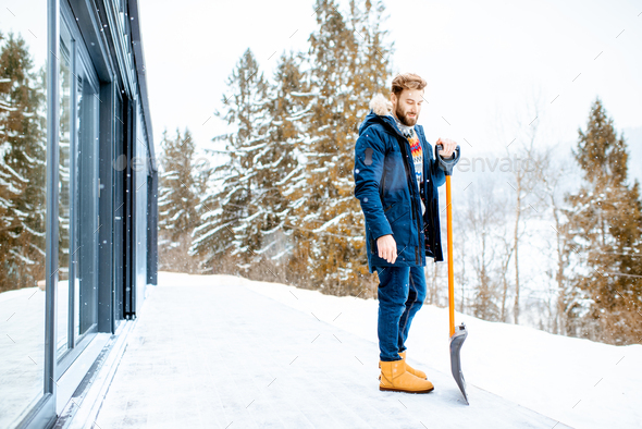 Portrait of a man in winter clothes with a snow shovel near the