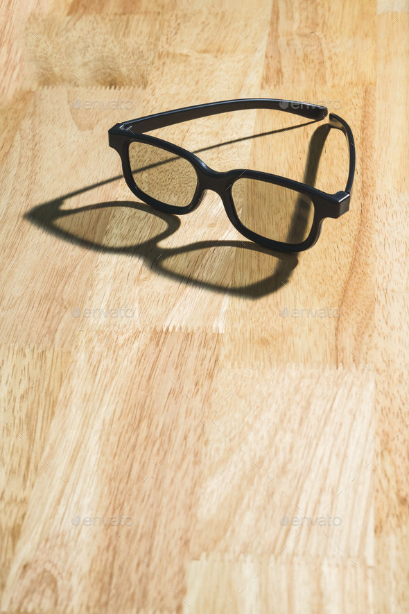 Black eyeglasses lay on wood table with shadow