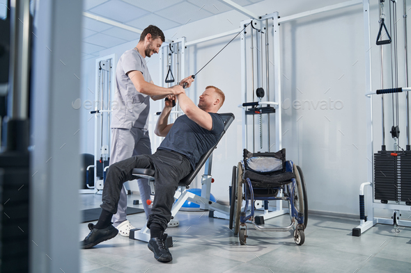 Man with disability pulls stretching strap with help of therapist