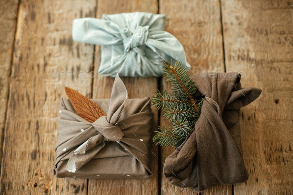 Stylish christmas gift wrapped in fabric on rustic table with